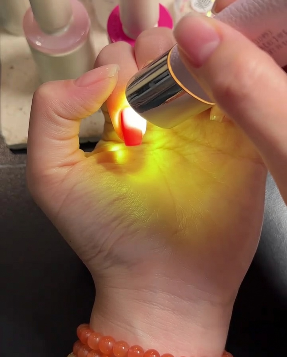 Eine Hand liegt unter einer tragbaren LED-Lampe und die gelbeschichteten Nägel härten aus.