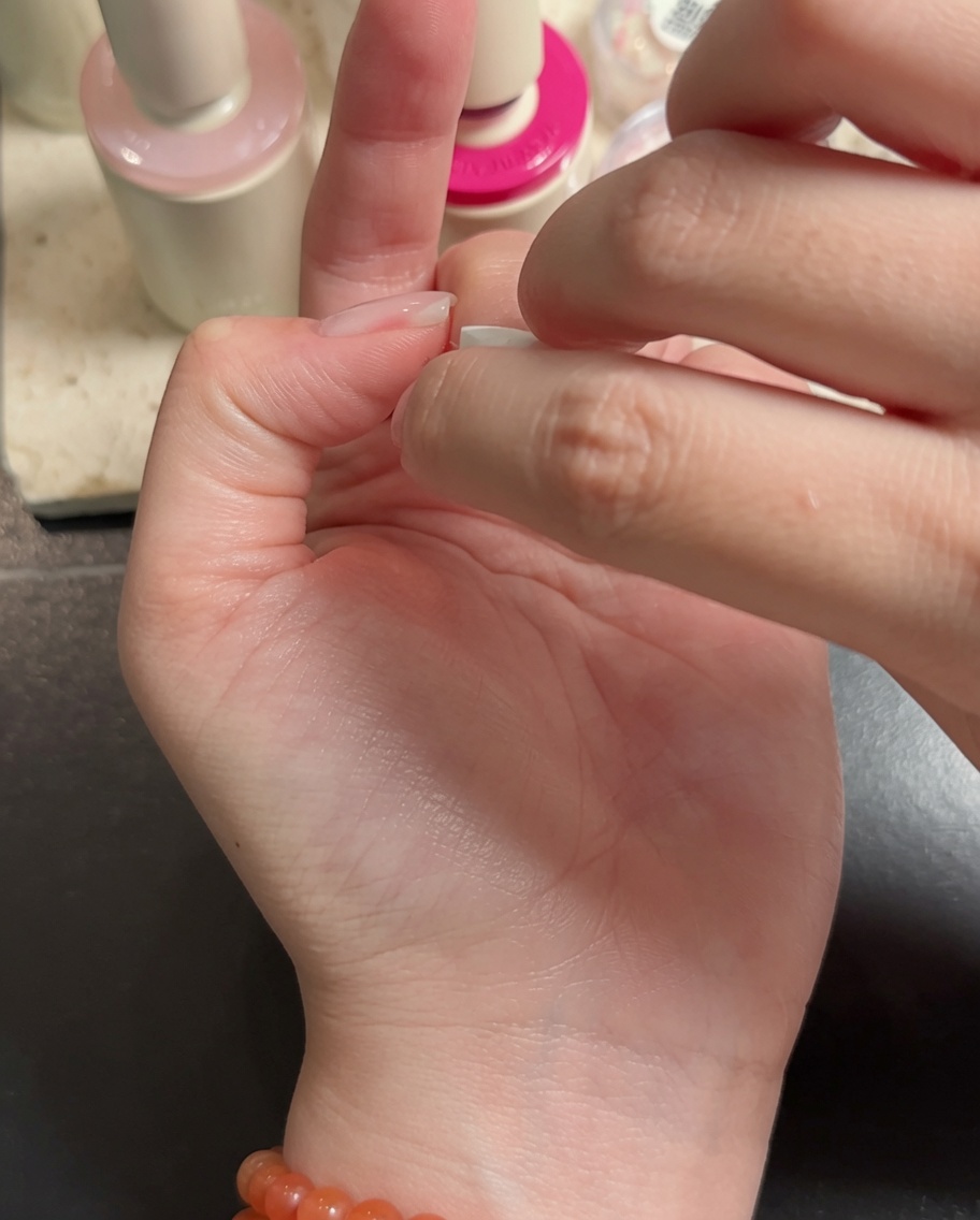 Ein Nail-Art-Pinsel trägt weißes Gel auf die Spitzen von Mittel- und Ringfinger auf, um einen Verlaufseffekt zu erzielen.