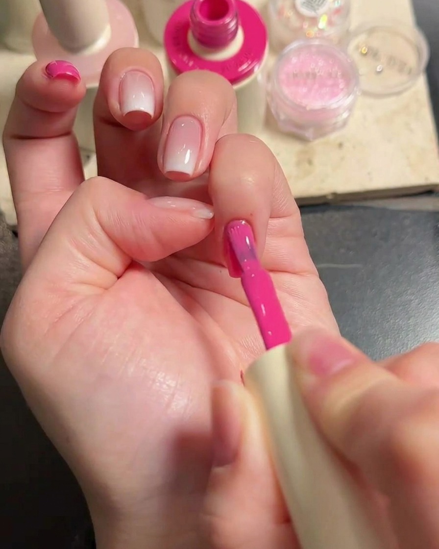Nahaufnahme einer Hand, die mit einem Nagelpinsel kräftiges rosa Gel auf die restlichen Fingernägel aufträgt.