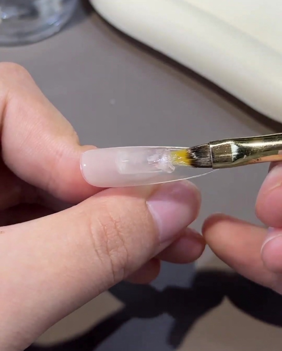 Eine Hand, die einen Nagel-Tip unter das Licht einer professionellen UV/LED-Nagellampe hält.