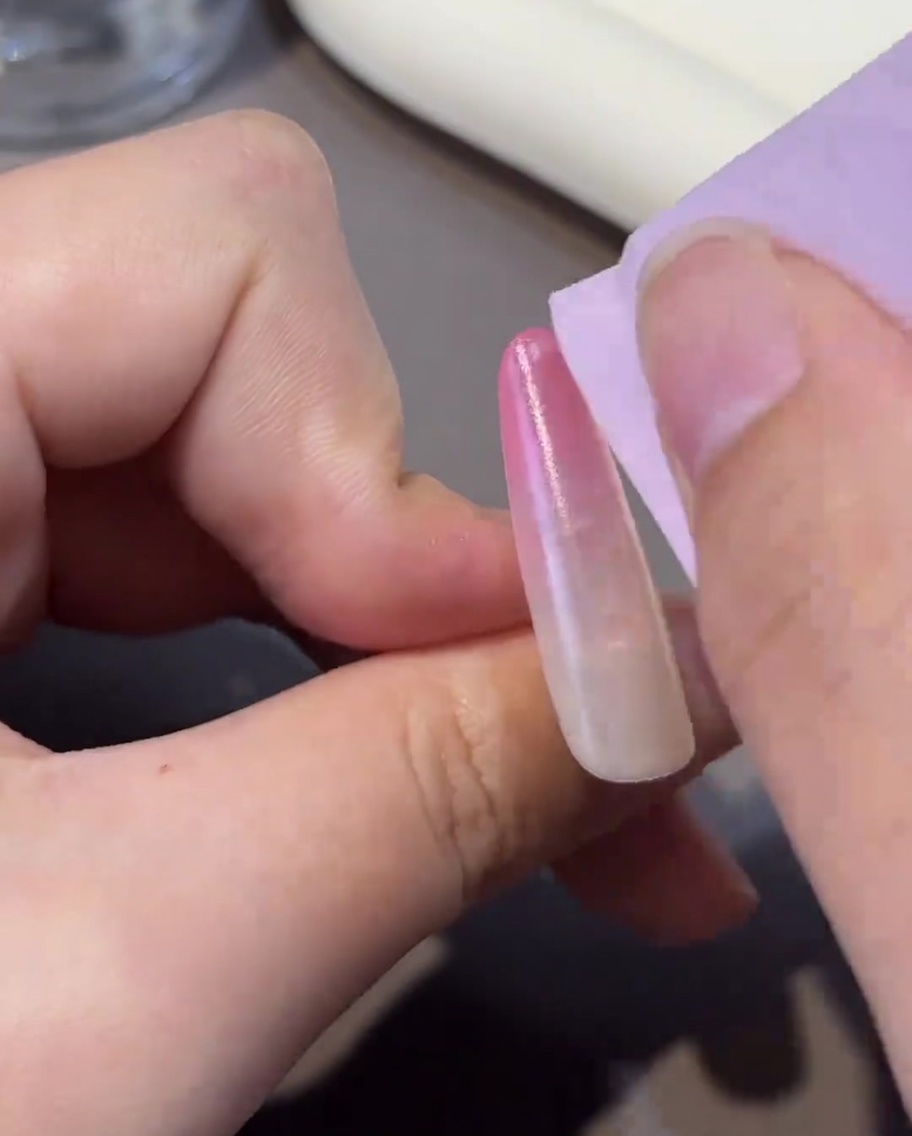 Ein fusselfreies Tuch reinigt die Oberfläche eines ausgehärteten Nagels und hinterlässt sie sauber für den nächsten Schritt.