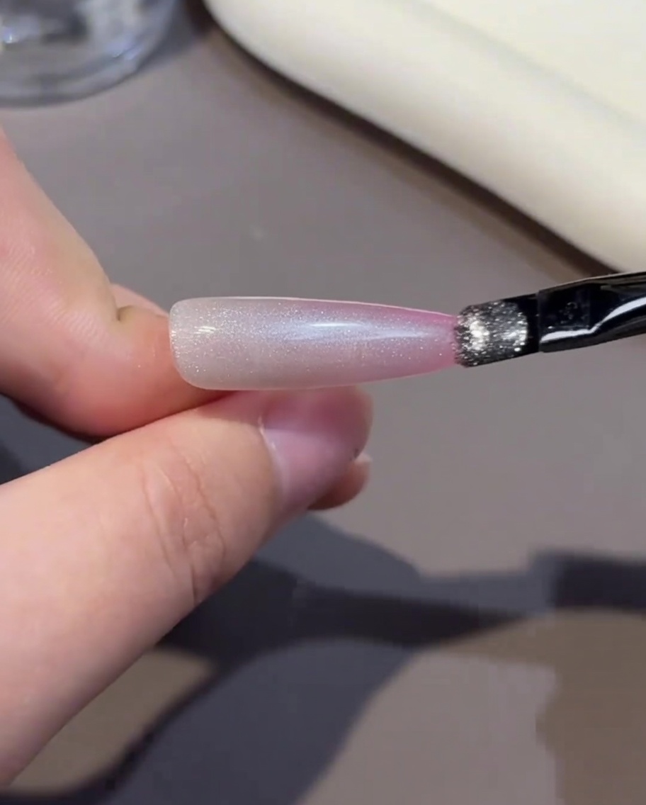 Ein Pinsel trägt eine Schicht rosa Gel-Nagellack auf die Nagelspitze auf.