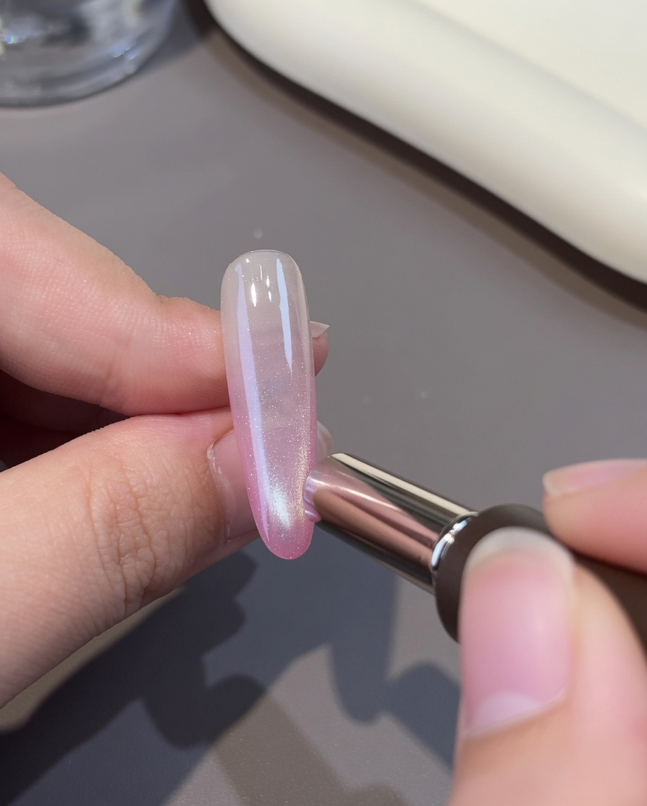 Eine Schicht weißes Cat-Eye-Gel wird über die rosa Basis des Nagels aufgetragen.