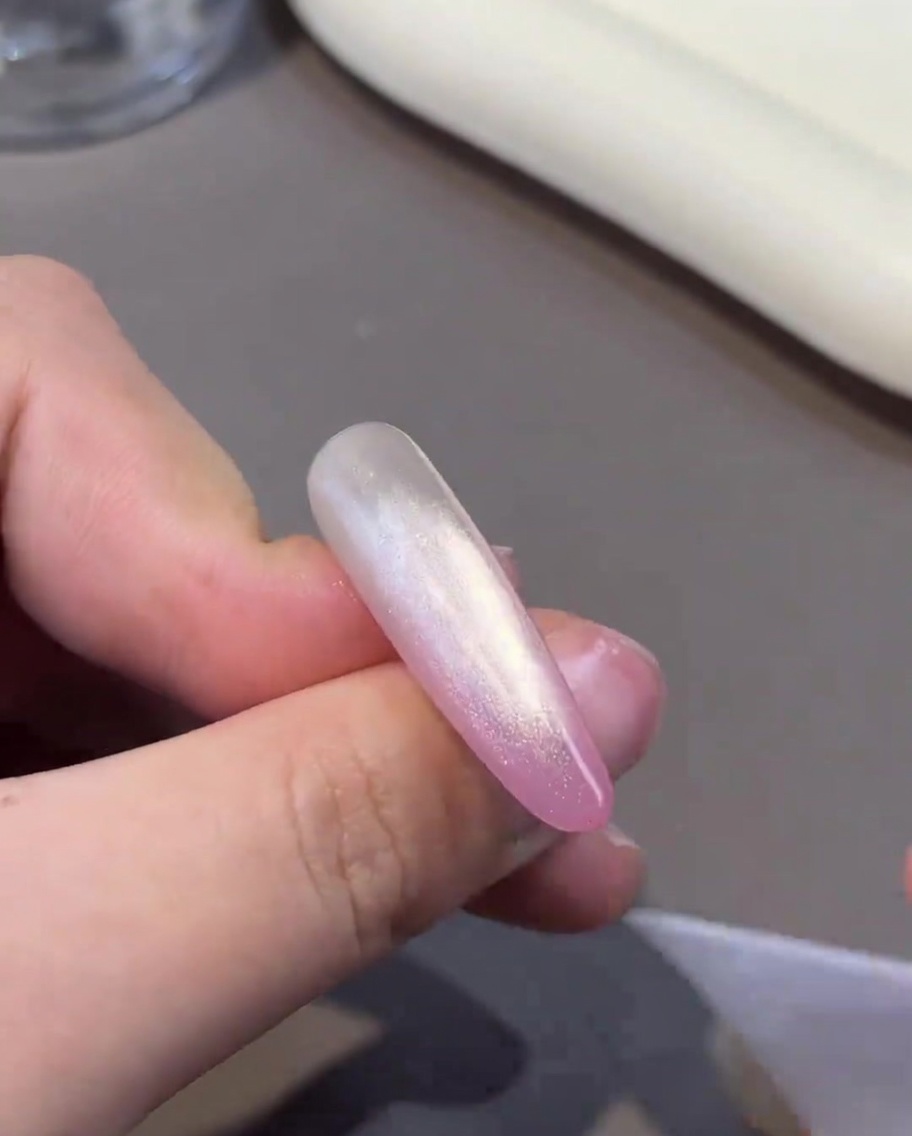 Ein Magnet wird nahe an den Nagel gehalten, um die Partikel im feuchten Cat-Eye-Gel zu verschieben.