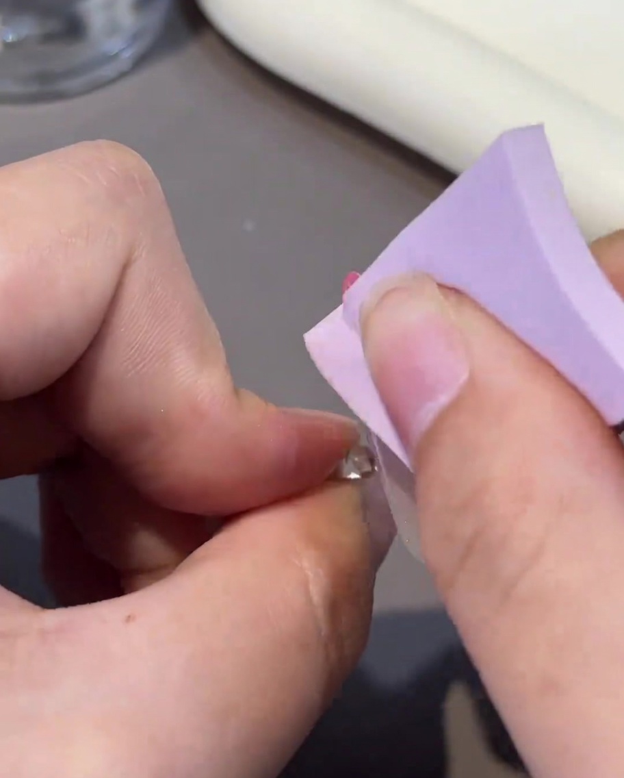 Eine fusselfreie Zellette reinigt die Oberfläche eines ausgehärteten Gelnagels.