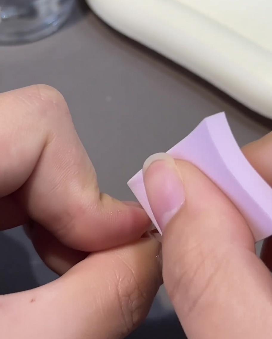 Nahaufnahme eines rosa Ombré-Nagels, der mit einer zweiten Schicht rosa Gel-Nagellack mittels eines kleinen Pinsels überzogen wird.