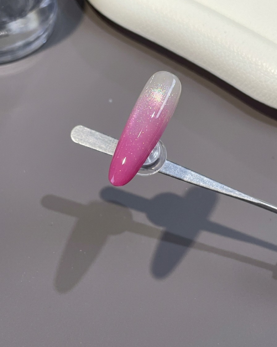 Ein Pinsel trägt einen klaren, glänzenden Topcoat auf einen fertigen rosa Ombré-Nagel auf.
