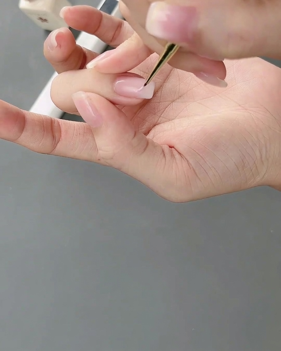 Ein feiner Nailart-Pinsel trägt hellrosa Gel in unregelmäßigen Blöcken auf den Nagel auf.