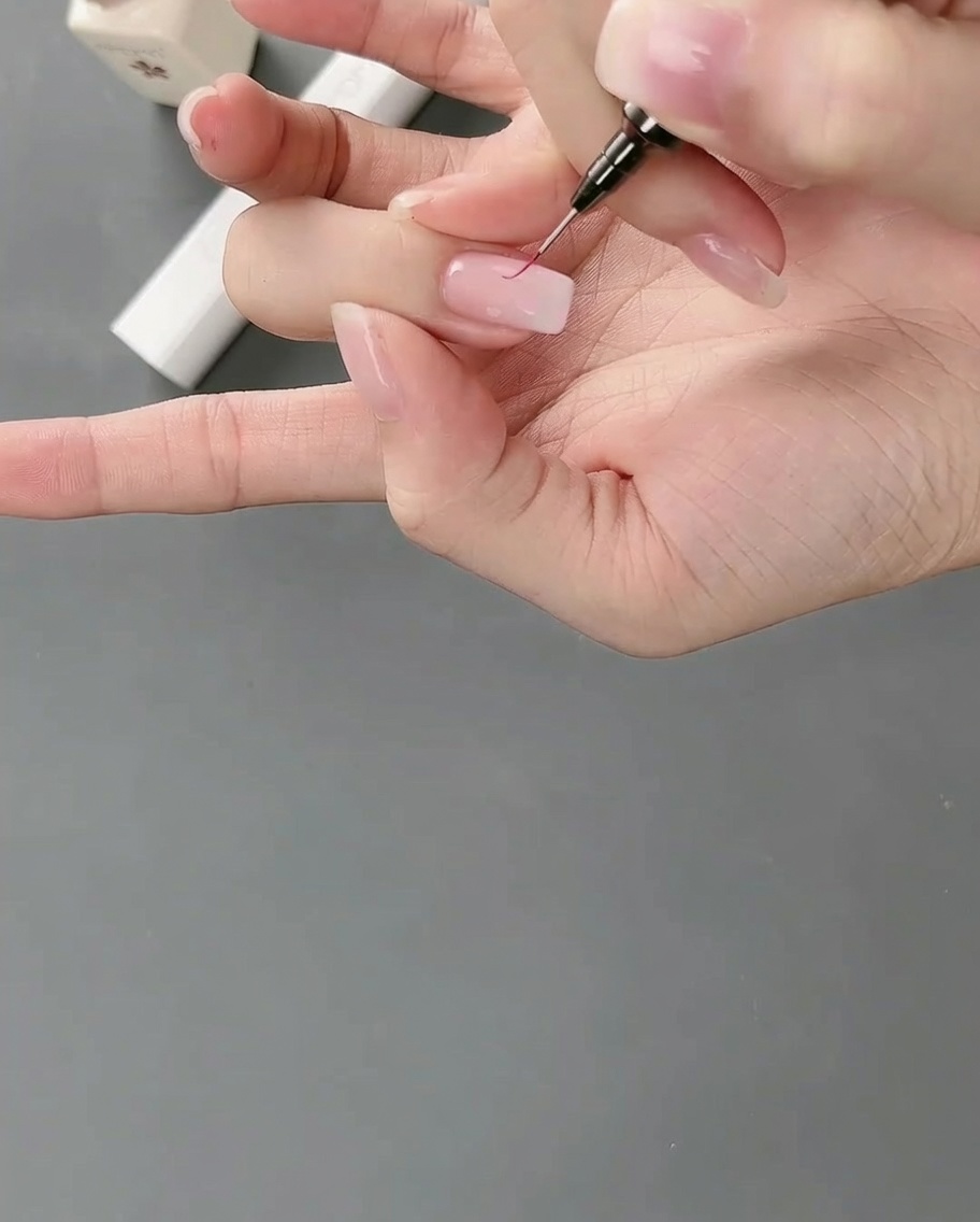 Ein Liner-Pinsel zieht feine Linien an den Kanten eines rosafarbenen Gelblocks auf dem Nagel.