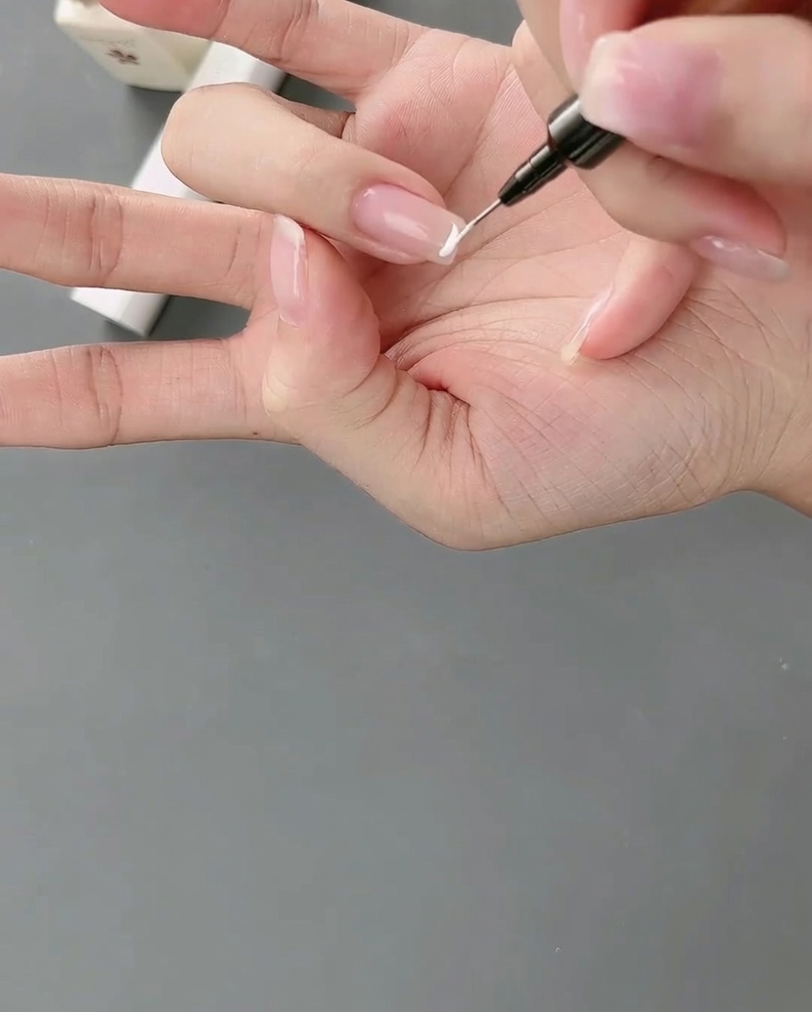 Ein Liner-Pinsel zieht eine präzise weiße Linie für ein hoch positioniertes French-Design.