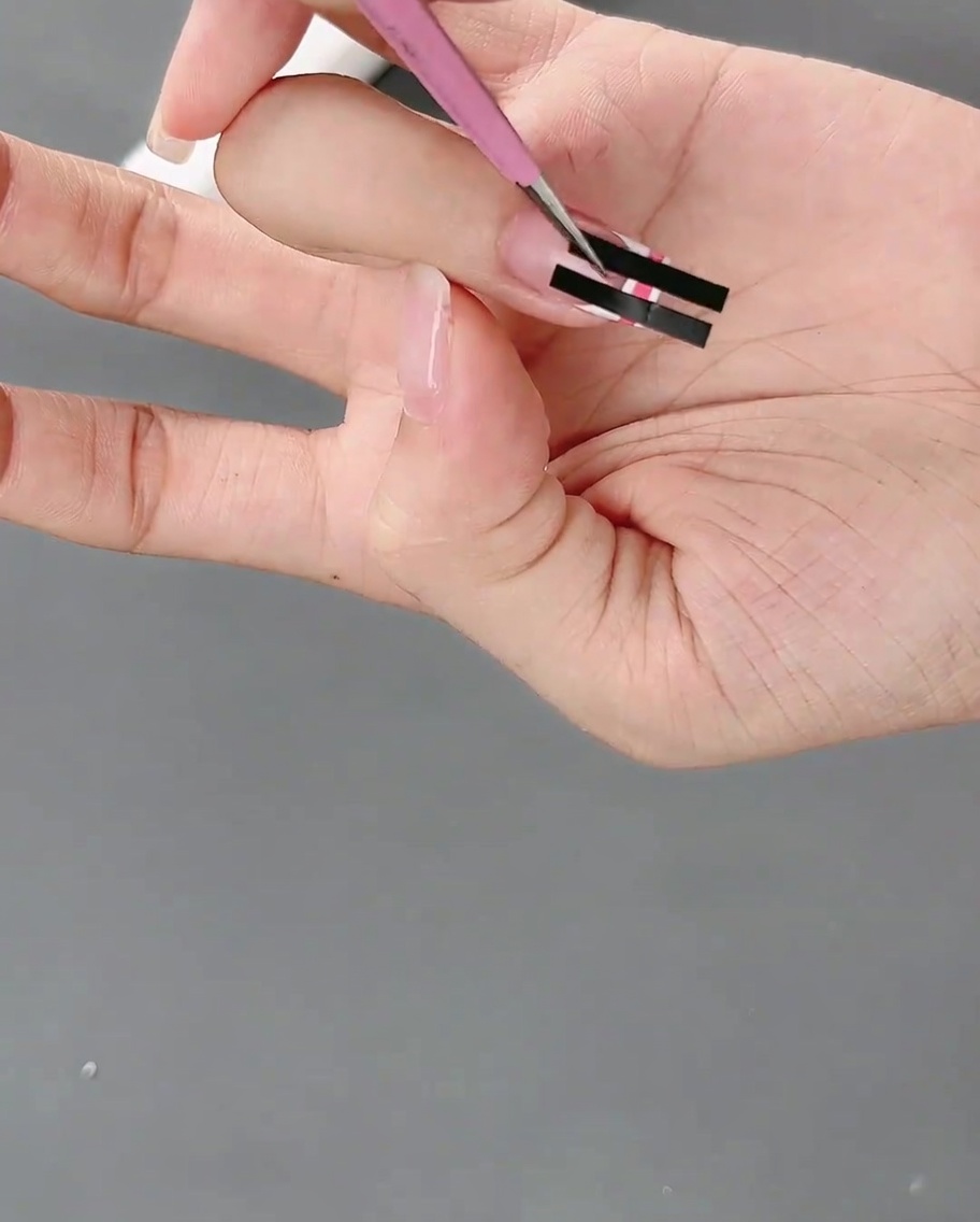 Eine Pinzette zieht vorsichtig einen Sticker ab und zeigt das karierte Muster darunter.