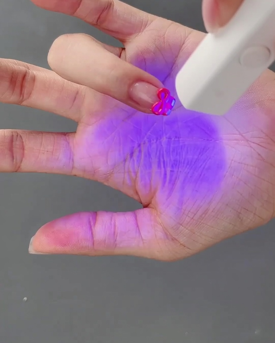 Eine Hand mit der frisch geformten 3D-Schleife härtet unter einer UV-Lampe aus.