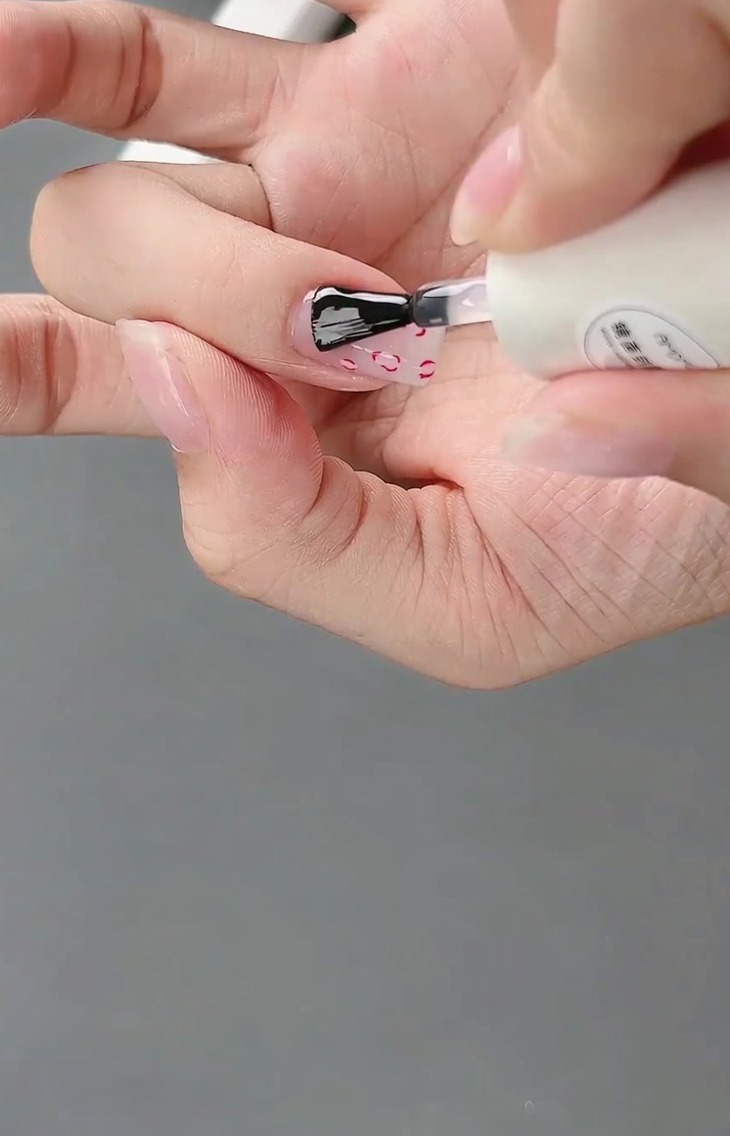 Ein Pinsel trägt glänzenden Top Coat über das fertige Design mit French Tip und 3D-Schleife auf.
