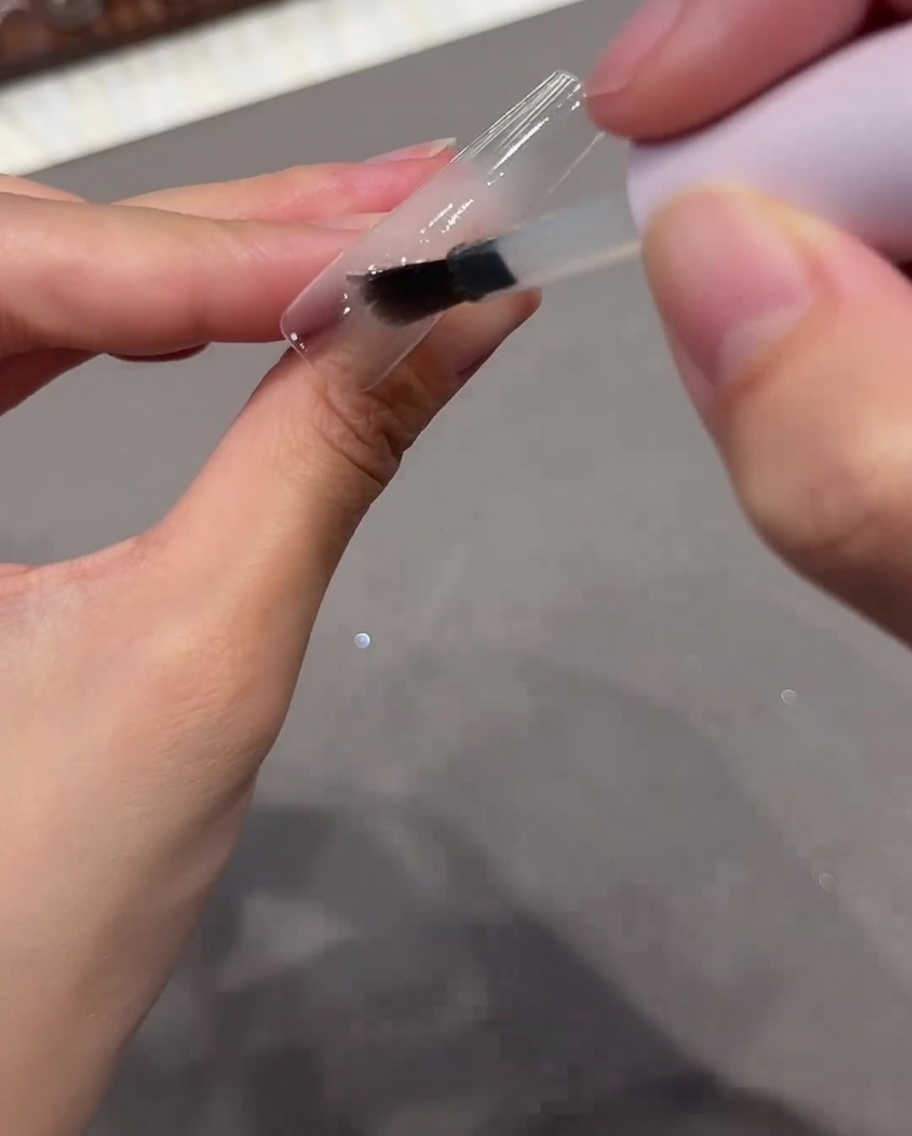 Ein Pinsel trägt klares Base-Coat-Gel auf einen klaren Nagel-Tip auf.