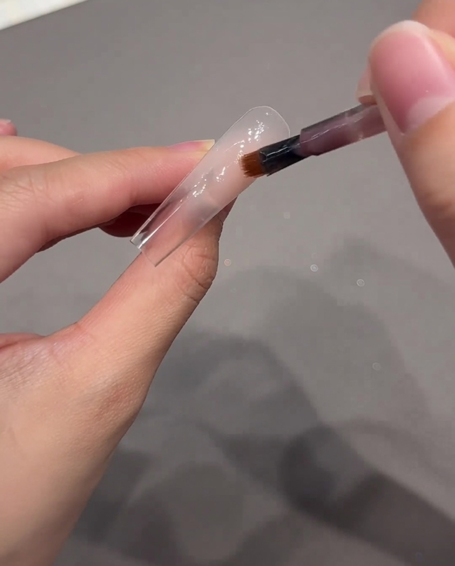 Ein Nailart-Pinsel trägt einen Punkt nudefarbenes rosa Gel auf den hinteren Bereich des Nagel-Tips auf.