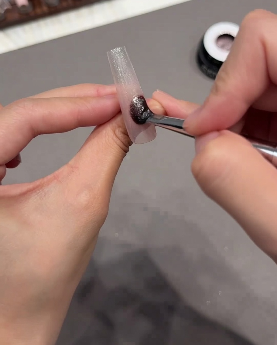 Ein Pinsel trägt schimmerndes Cat-Eye-Gel auf die gesamte Oberfläche des Nagel-Tips auf.