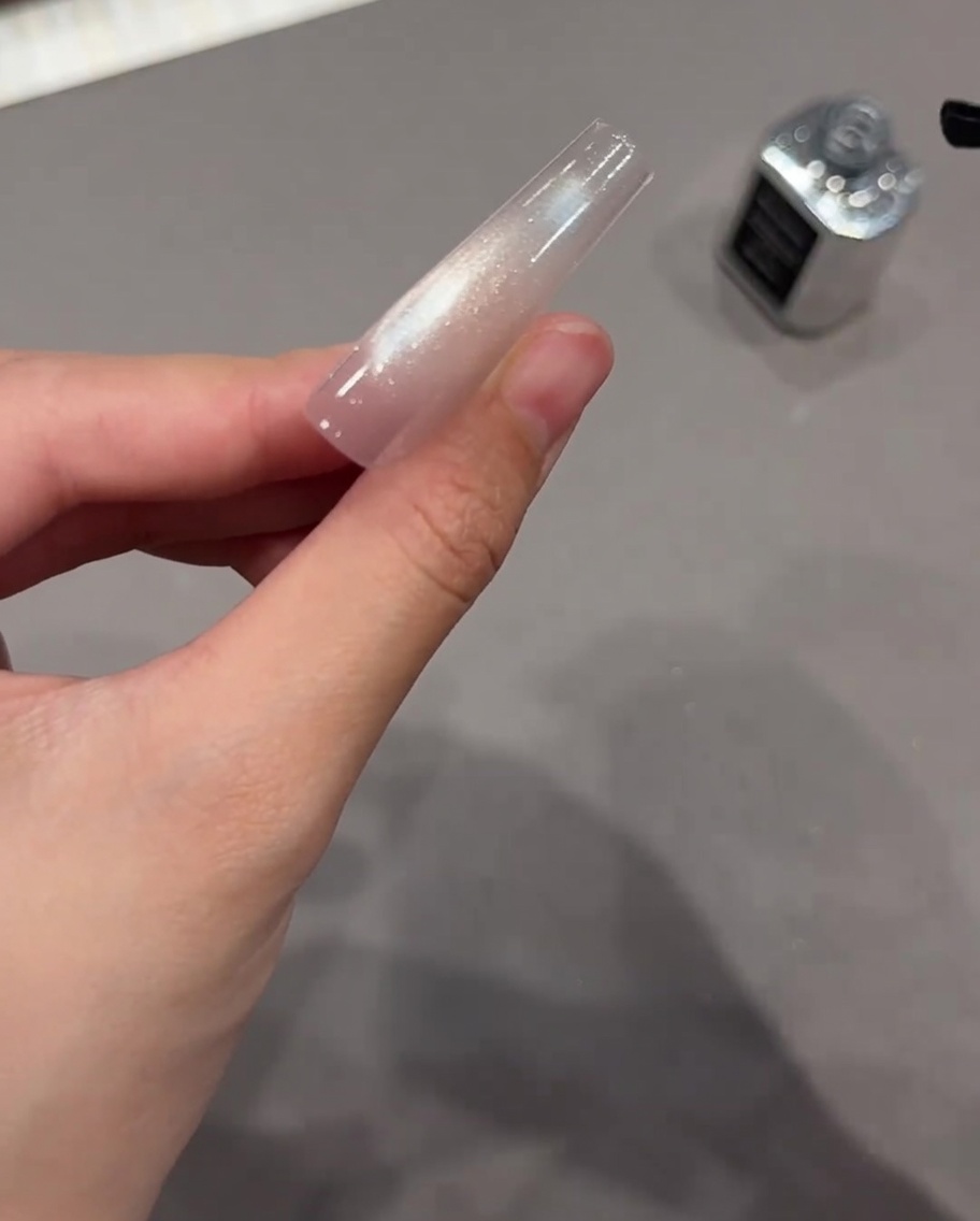 Ein schwarzer Nagelpinsel trägt klaren Top Coat über einen ausgehärteten Cat-Eye-Nagel auf.