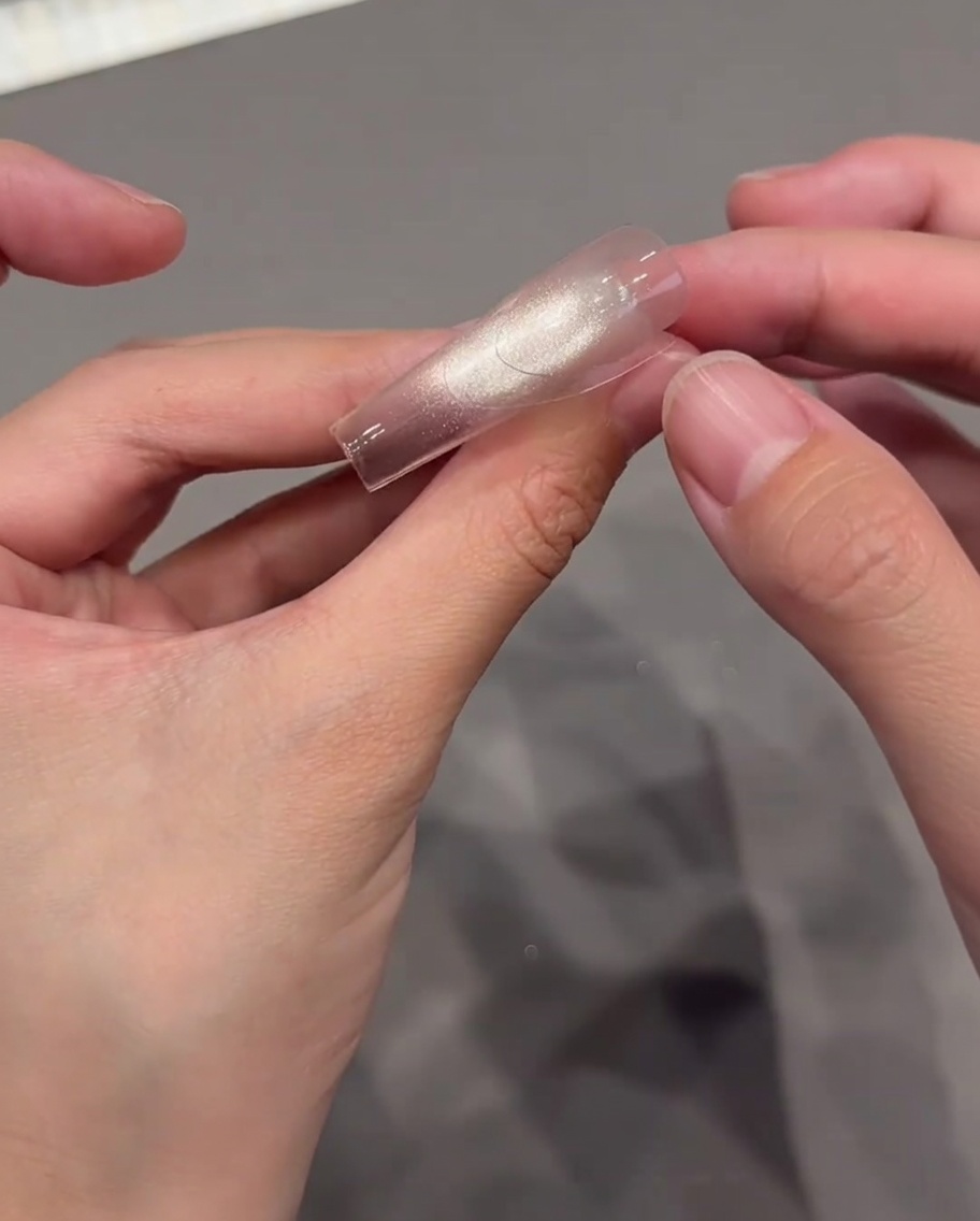 Daumen platzieren vorsichtig einen transparenten, geschwungenen French-Tip-Sticker auf einen glänzenden Nagel.