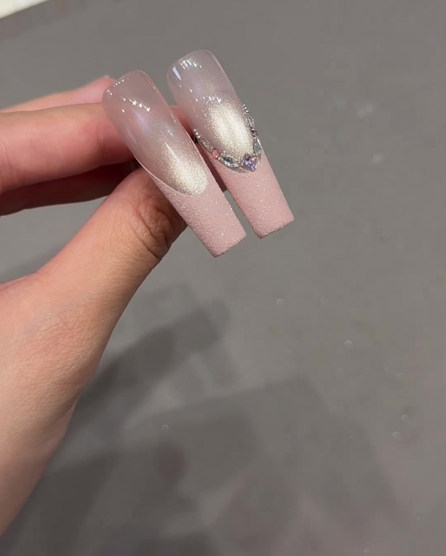 Nahaufnahme eines Nagels mit einem French-Design, bei dem verschiedene Strasssteine entlang der French-Linie angeordnet sind.