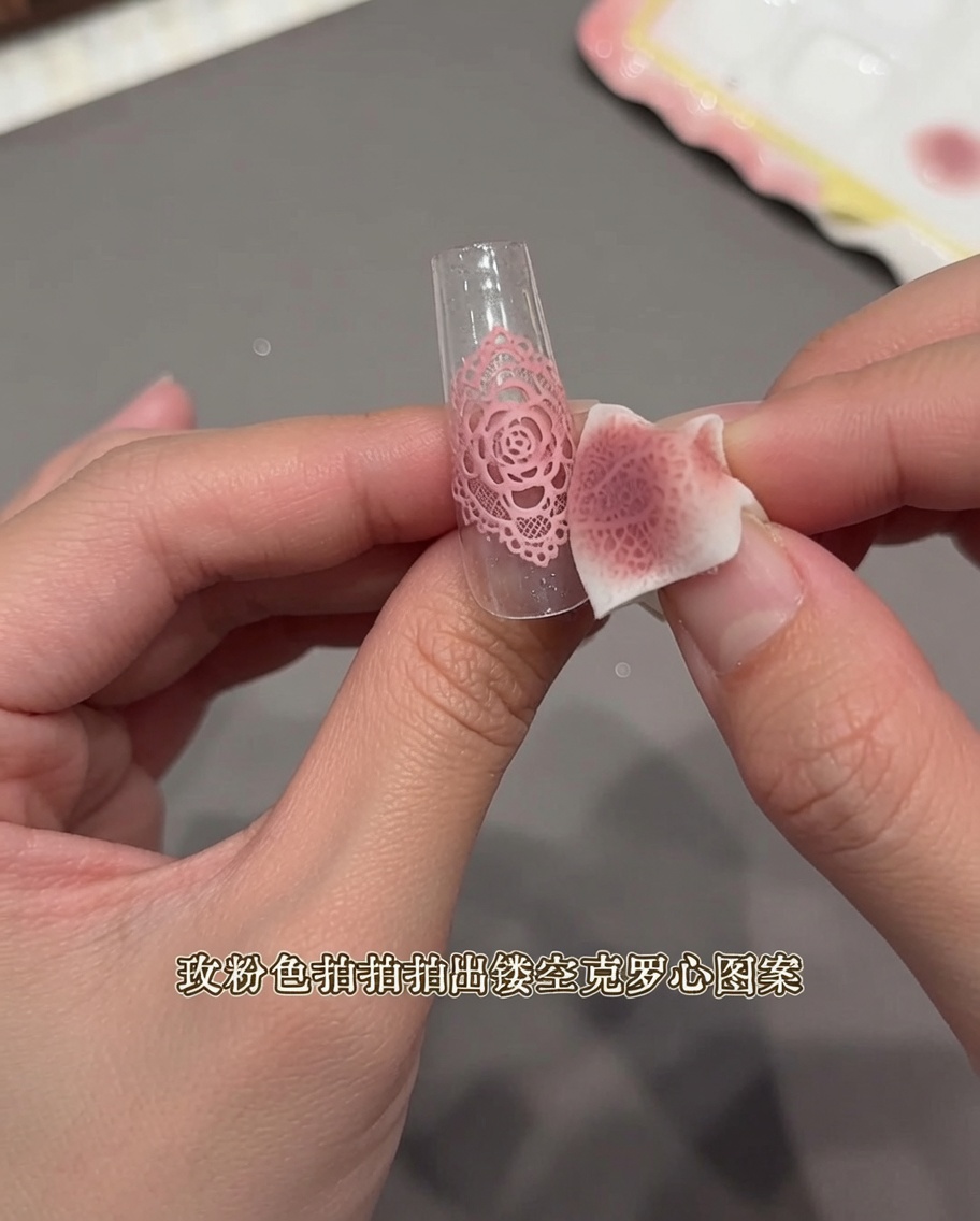 Nahaufnahme einer Hand, die mit einem Make-up-Schwamm über einen spitzenartigen Sticker auf einem klaren Nagel-Tip tupft.