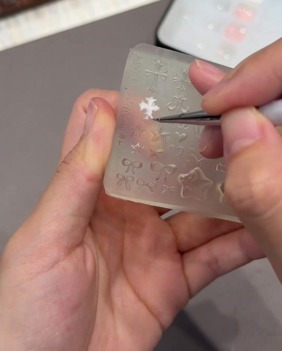 Eine Pinzette hält eine kleine weiße 3D-herzförmige Form, während sie darauf vorbereitet wird, auf einen Nagel platziert zu werden.