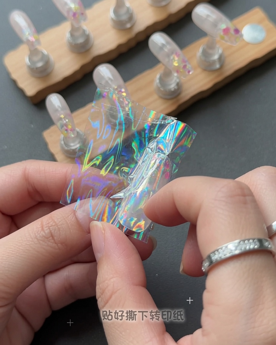 Eine Hand, die eine klare Kunststofffolie von einem Nagel abzieht, um ein holografisches Sternendesign zu enthüllen.