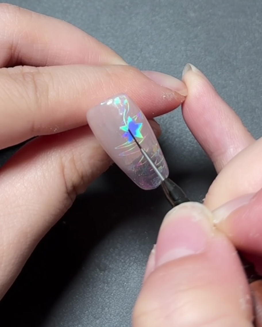 Ein Detailpinsel, der vibrierendes Farbgel in ein Sternendesign auf einem Nagel malt.
