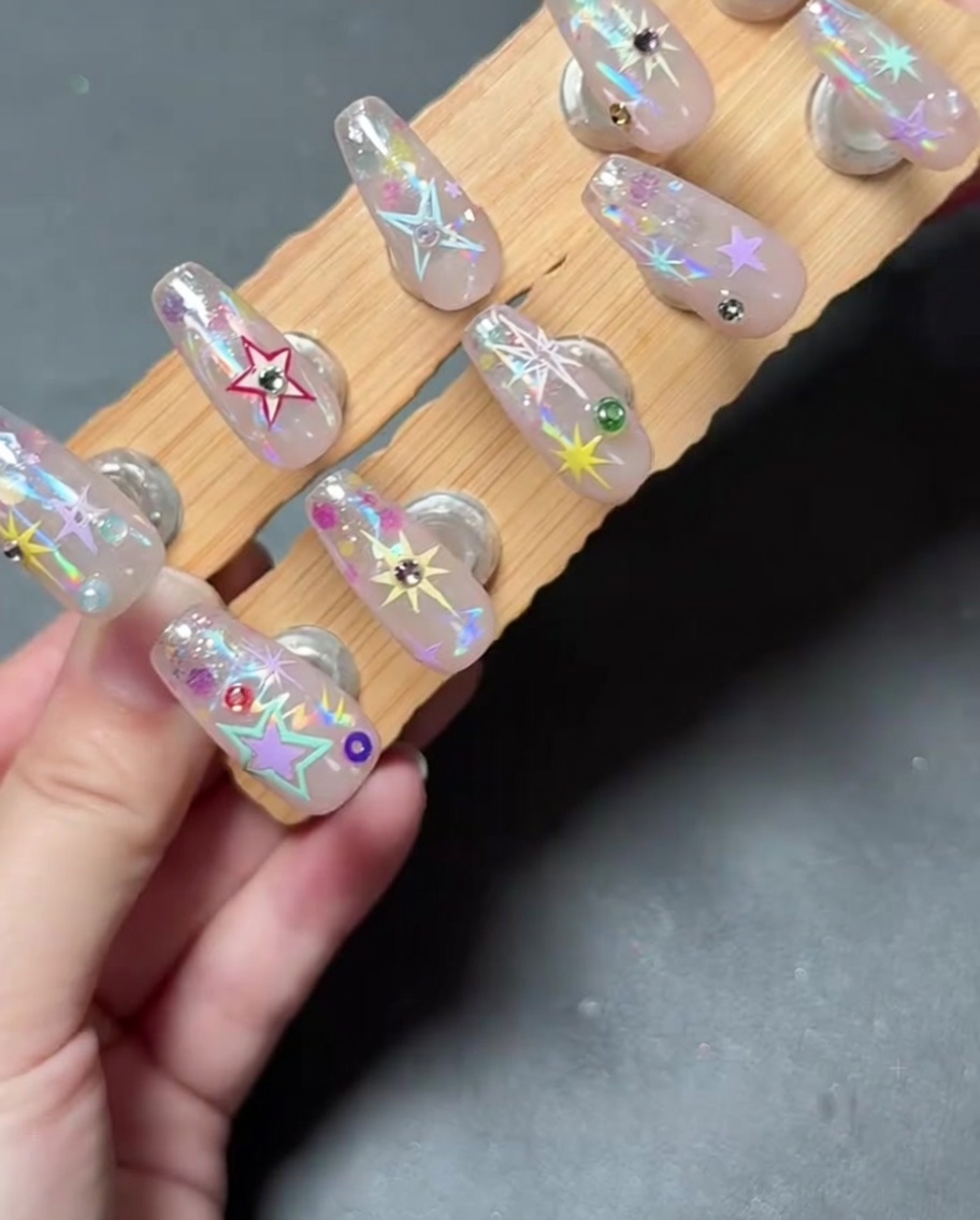 Nahaufnahme einer Hand, die mit einem Werkzeug einen kleinen Strassstein auf einem verzierten Nagel platziert.