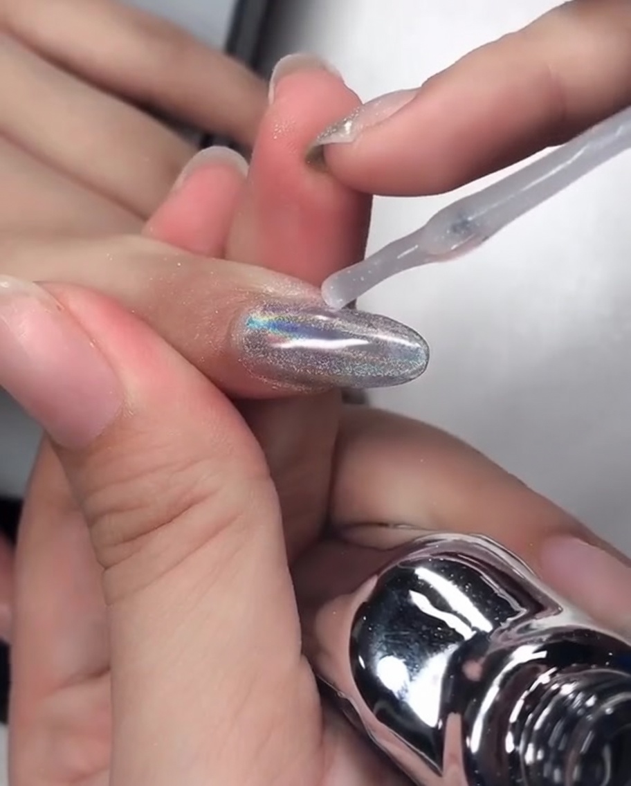 Ein Nagelpinsel trägt klares Aufbau-Gel auf einen verchromten Nagel auf und versiegelt die freie Kante.