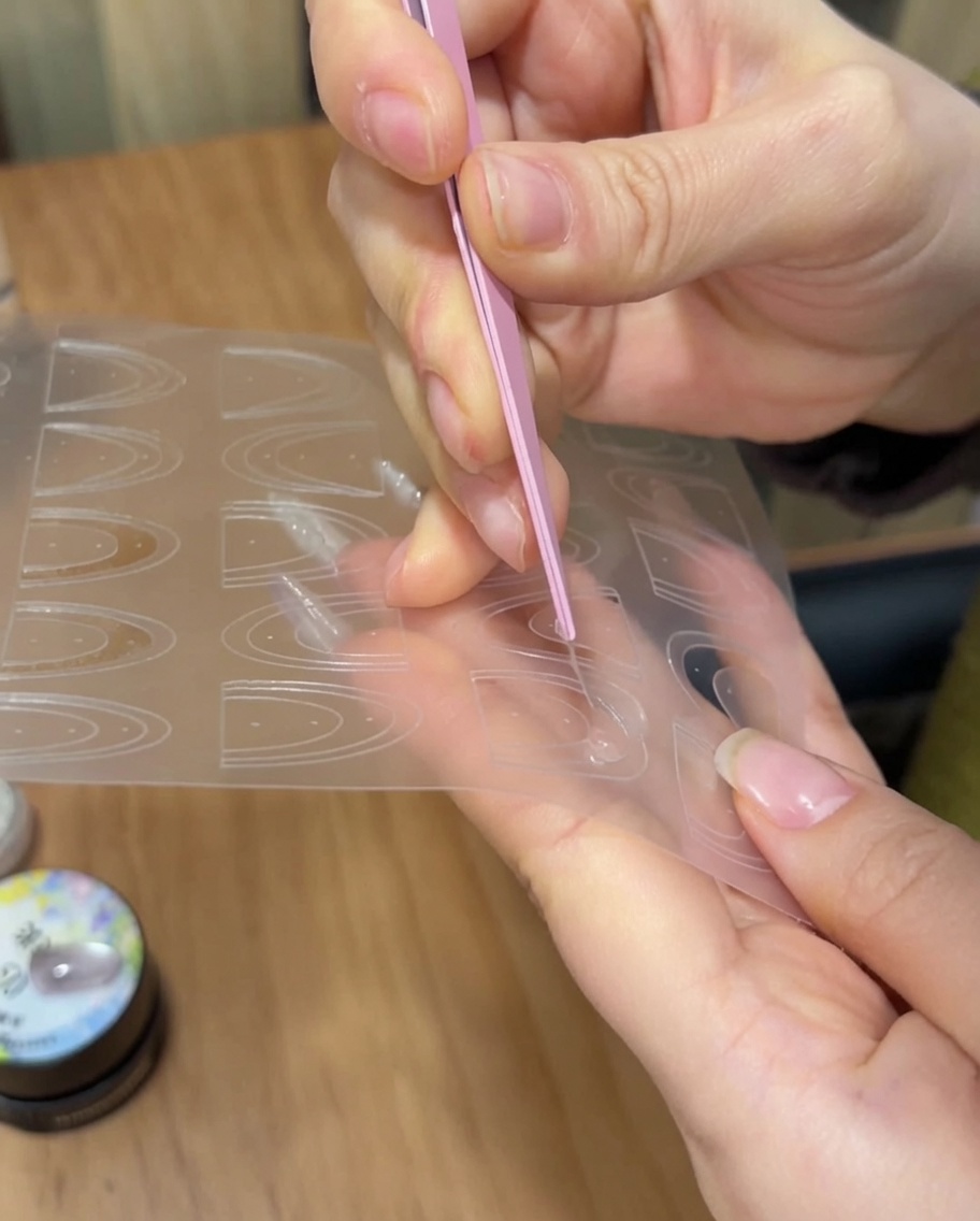 Eine Pinzette platziert einen dünnen French-Maniküre-Aufkleber auf der Spitze eines manikürten Nagels.