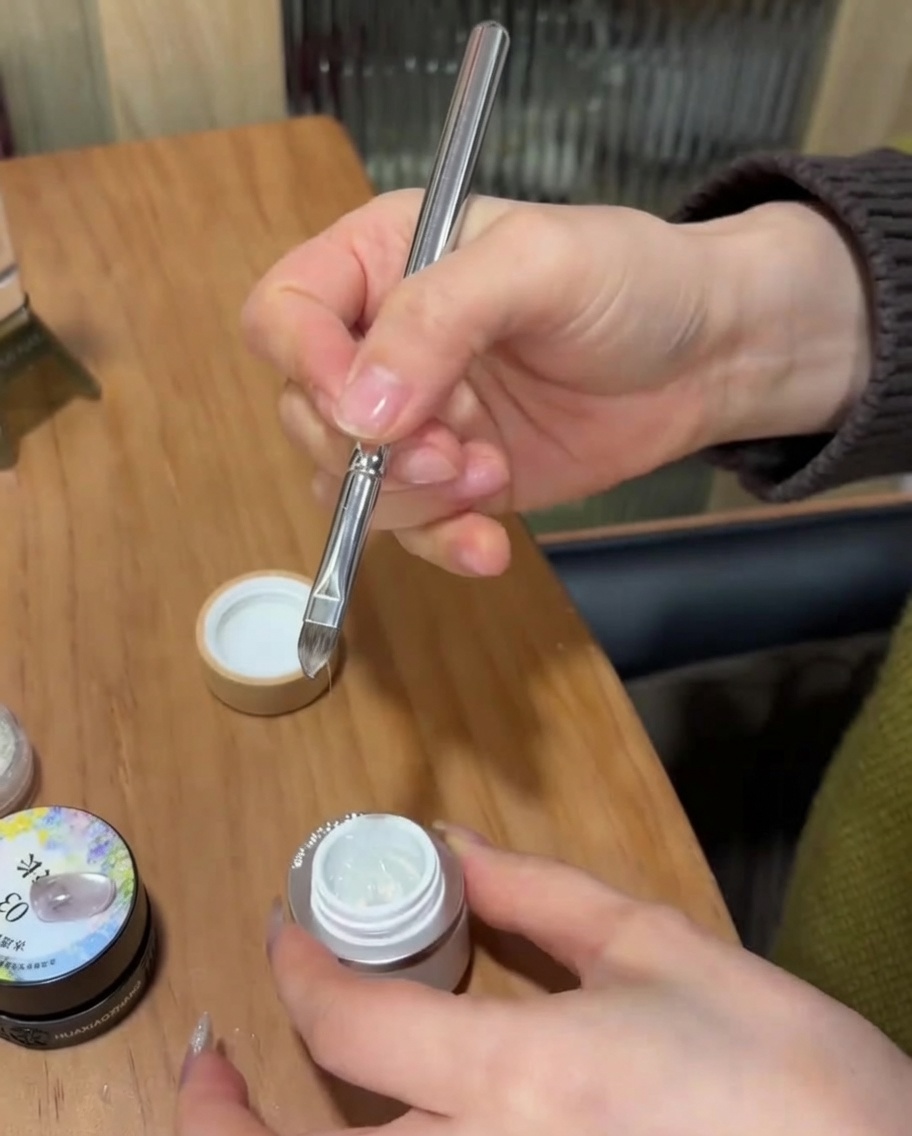 Ein Detailpinsel trägt klares Builder Gel über die Nagelspitze auf, die durch eine French-Schablone begrenzt ist.