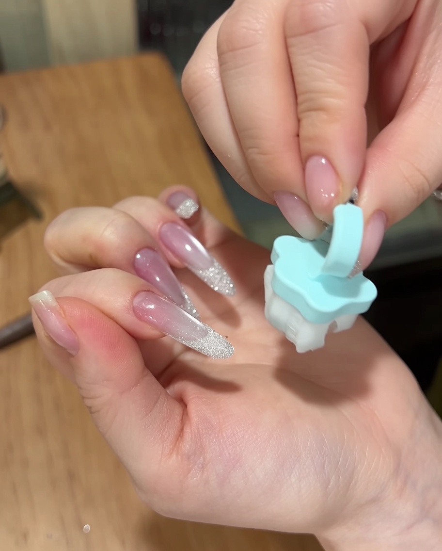 Eine Hand entfernt mit einem kleinen, weichen blauen Pinsel überschüssiges Sugar Powder von der Oberfläche einer fertigen Maniküre.