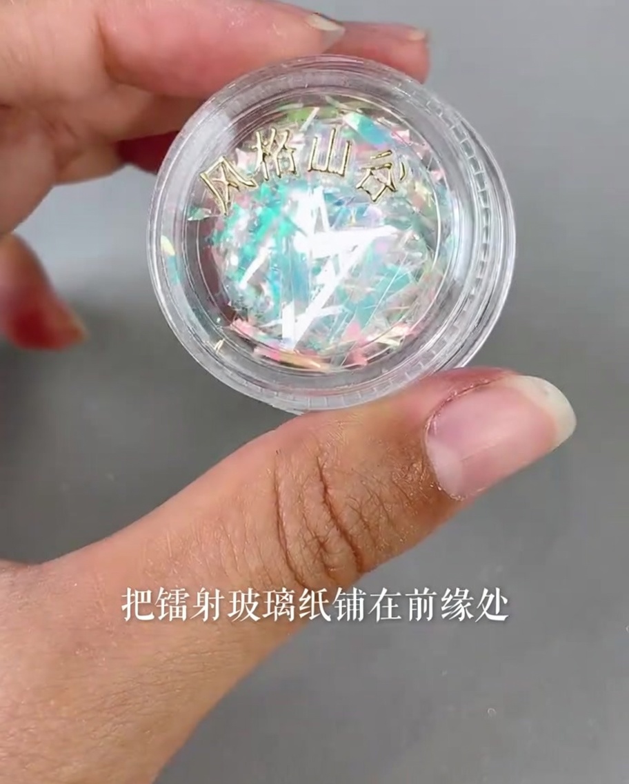 Winzige Stücke irisierender Laser-Glasfolie werden mit einer Pinzette auf die Kante eines Nageltips platziert.