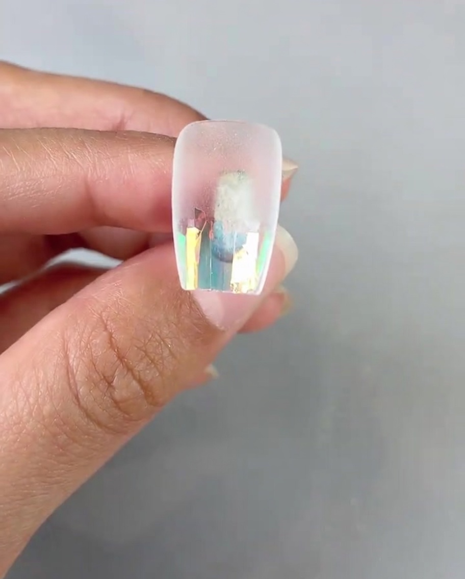 Ein Nagelpinsel trägt klaren Top-Gel über der Glasfolie auf dem Nageltip auf.