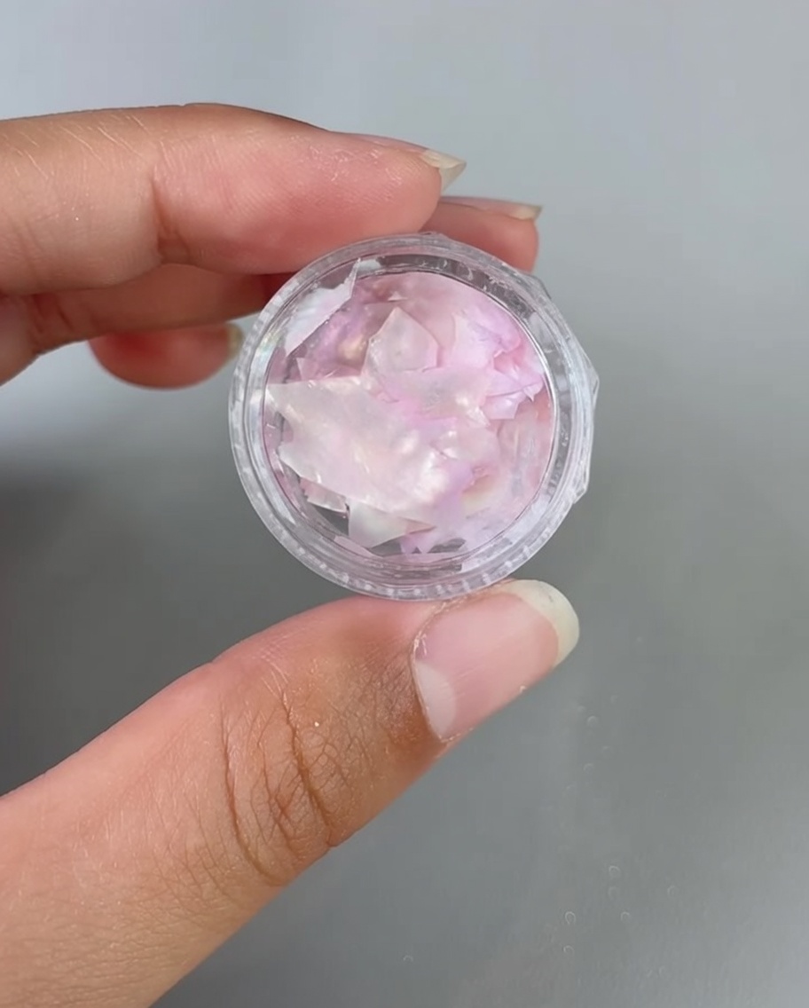 Pinzette platziert irisierende Muschelsplitter auf einen mit Gel beschichteten Nagel.