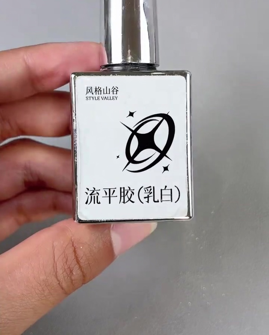 Ein kleiner Pinsel trägt einen Tropfen milchig-weißes Gel in die Ecke eines verzierten Nagels auf.