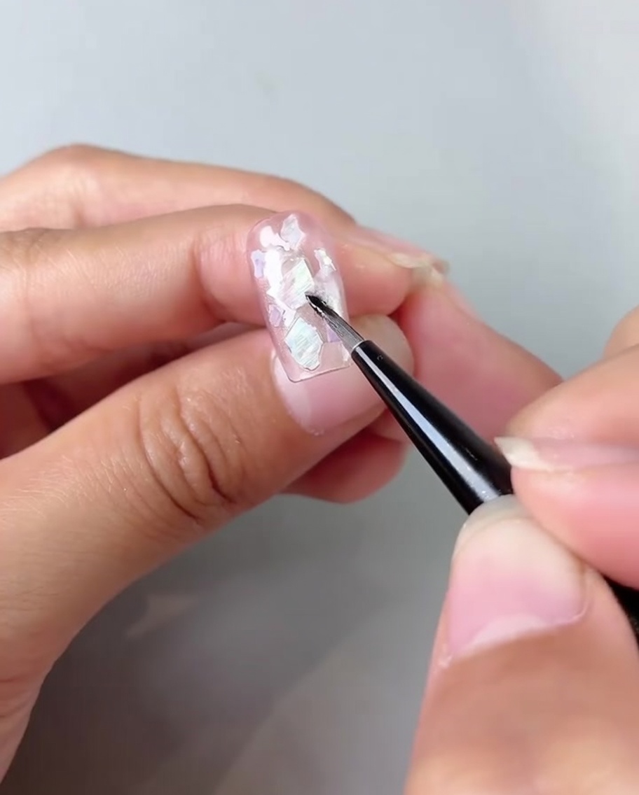 Ein Pinsel verblendet milchig-weißes Gel in die Ecken eines Pink Cat-Eye Nagels.