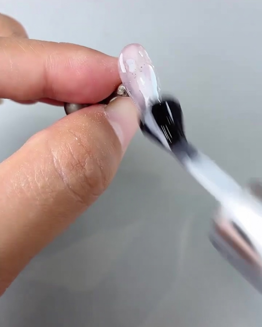 Ein Pinsel trägt glänzenden Top Coat über dem fertigen Nageldesign auf.