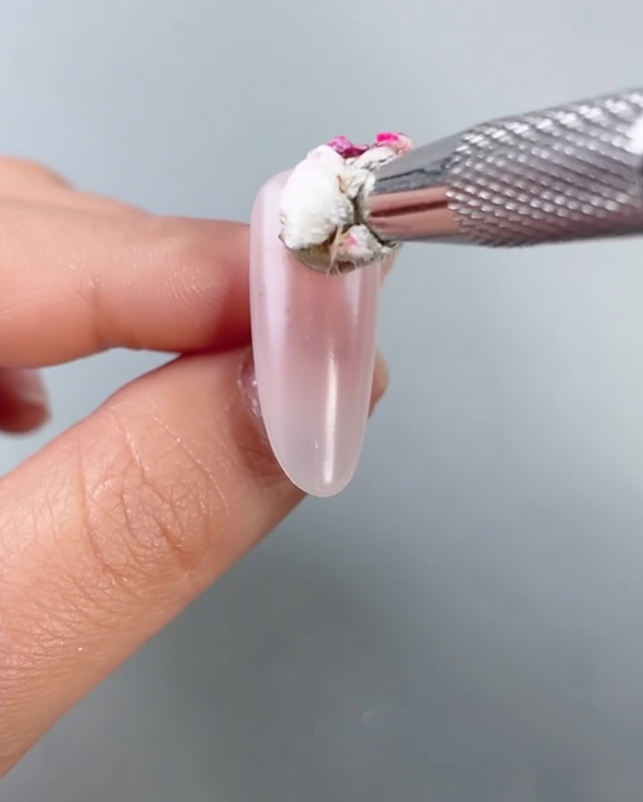 Nahaufnahme eines kleinen Schwämmchens, das leuchtend pinkes Gel auf die Mitte eines mandelförmigen Nagels tupft, um einen Rouge-Effekt zu erzielen.