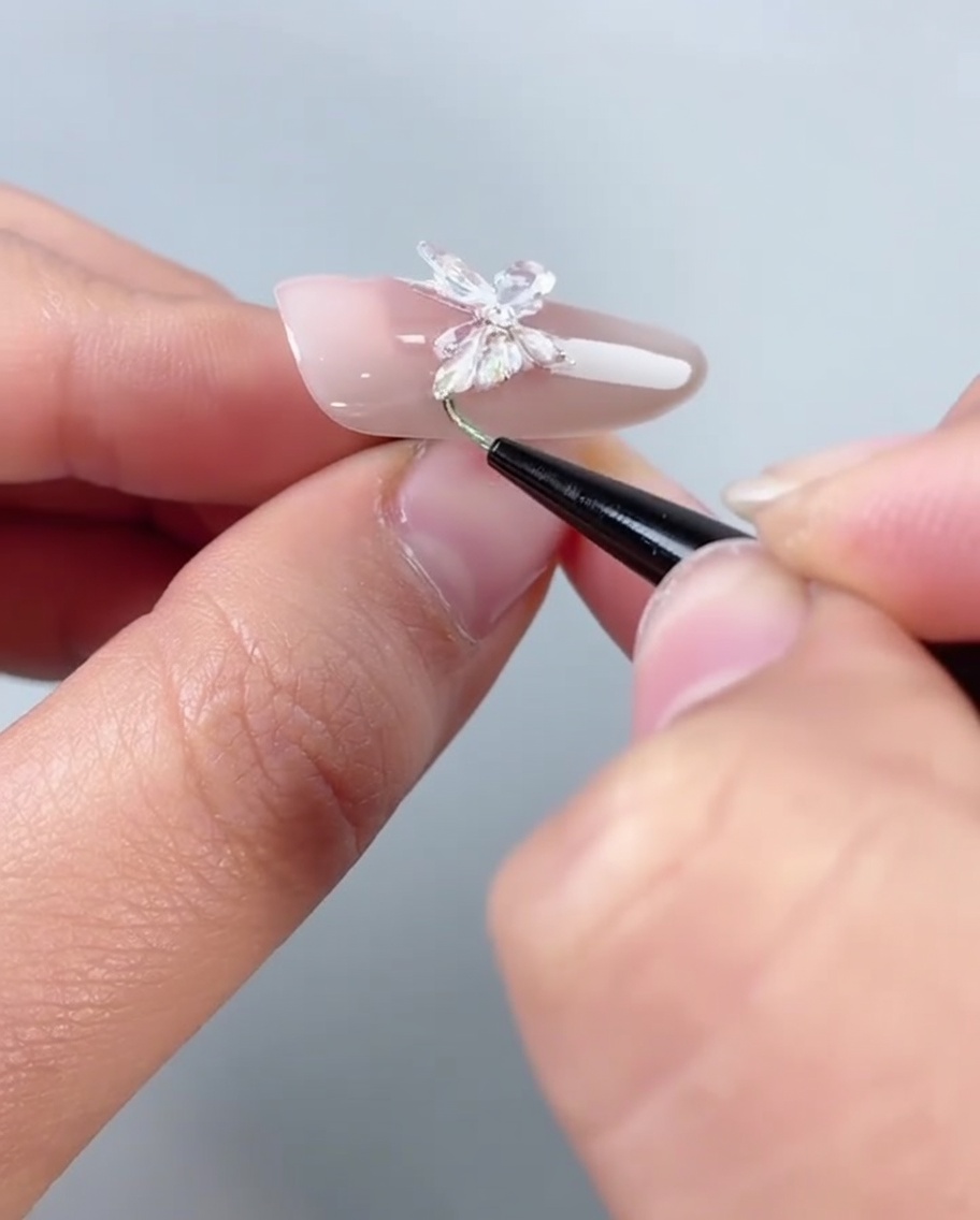 Ein Pinsel trägt klares Versiegelungsgel entlang der unteren Kante eines mit Schmetterlingen verzierten Nagels auf.