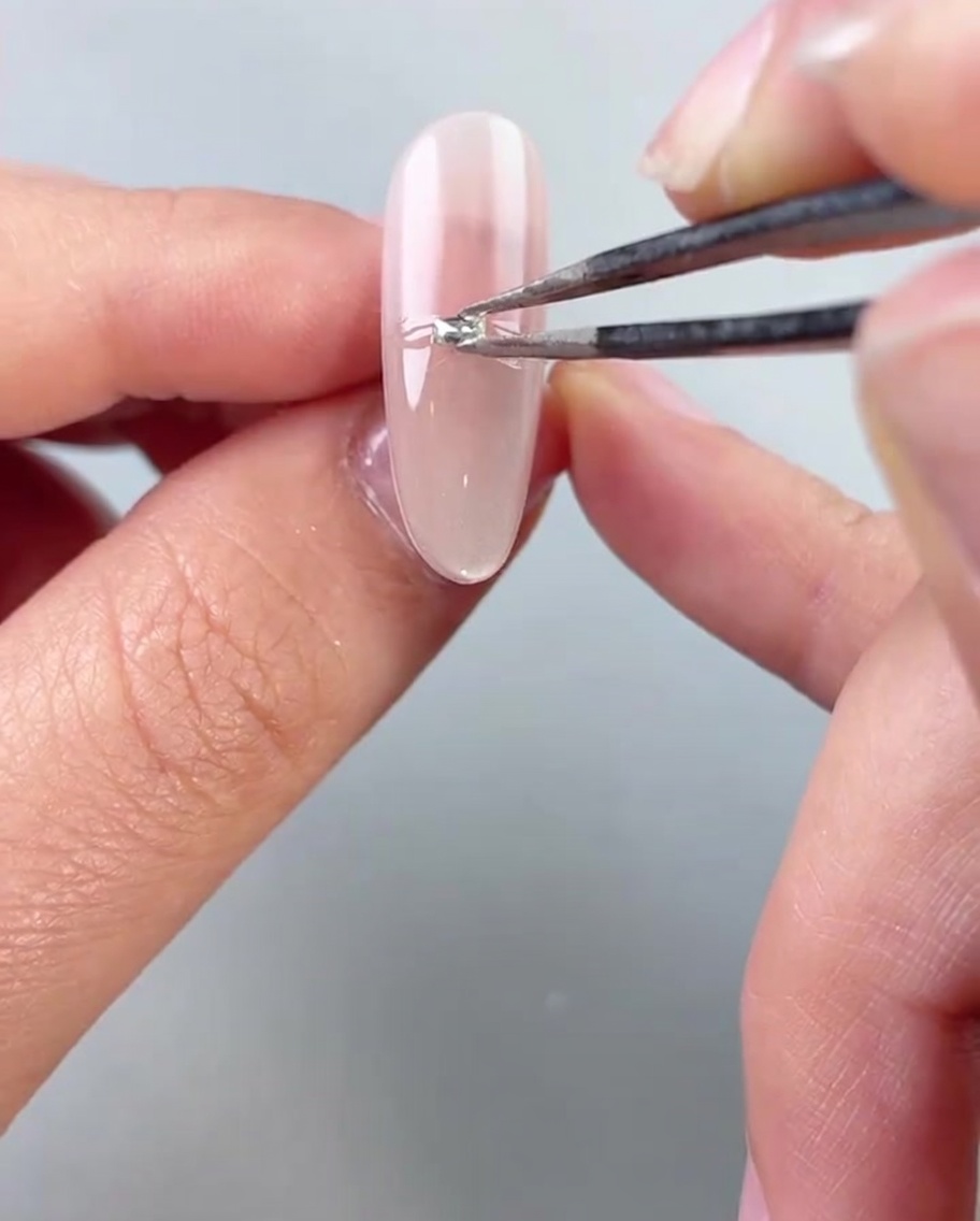 Eine Pinzette platziert kleine Silberperlen oder Strasssteine horizontal in der Mitte eines lackierten Nagels.