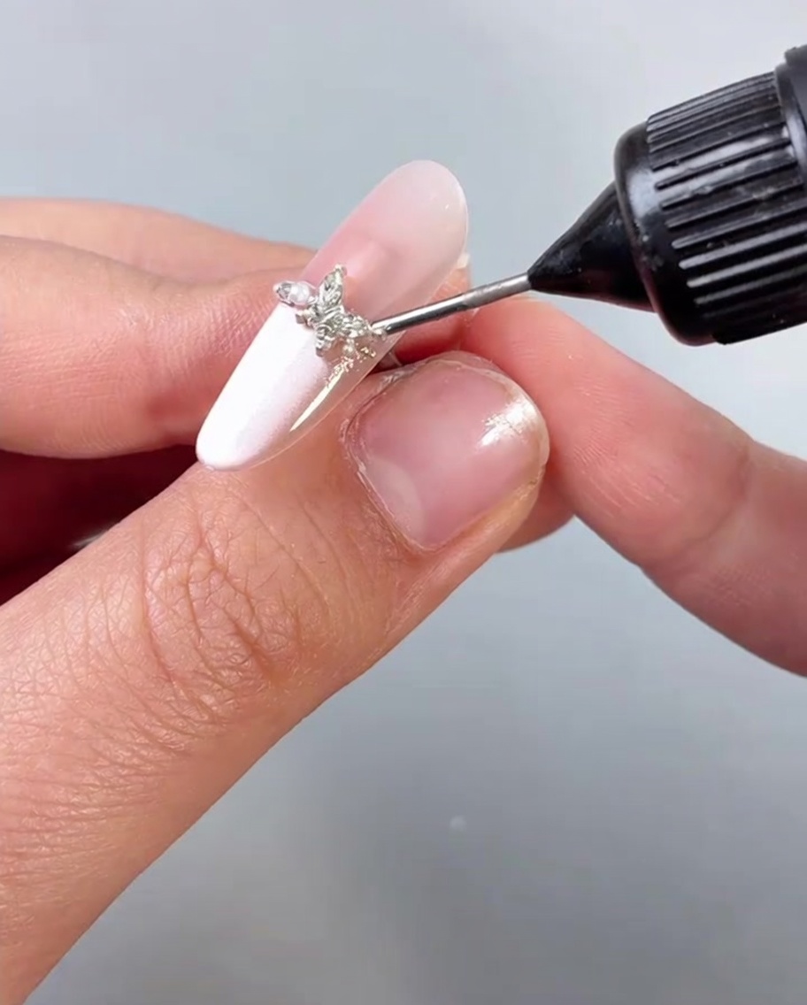 Auftragen eines klaren Top Coats oder einer Versiegelung über einen Fingernagel, der mit einem Schmetterlings-Charm verziert ist.