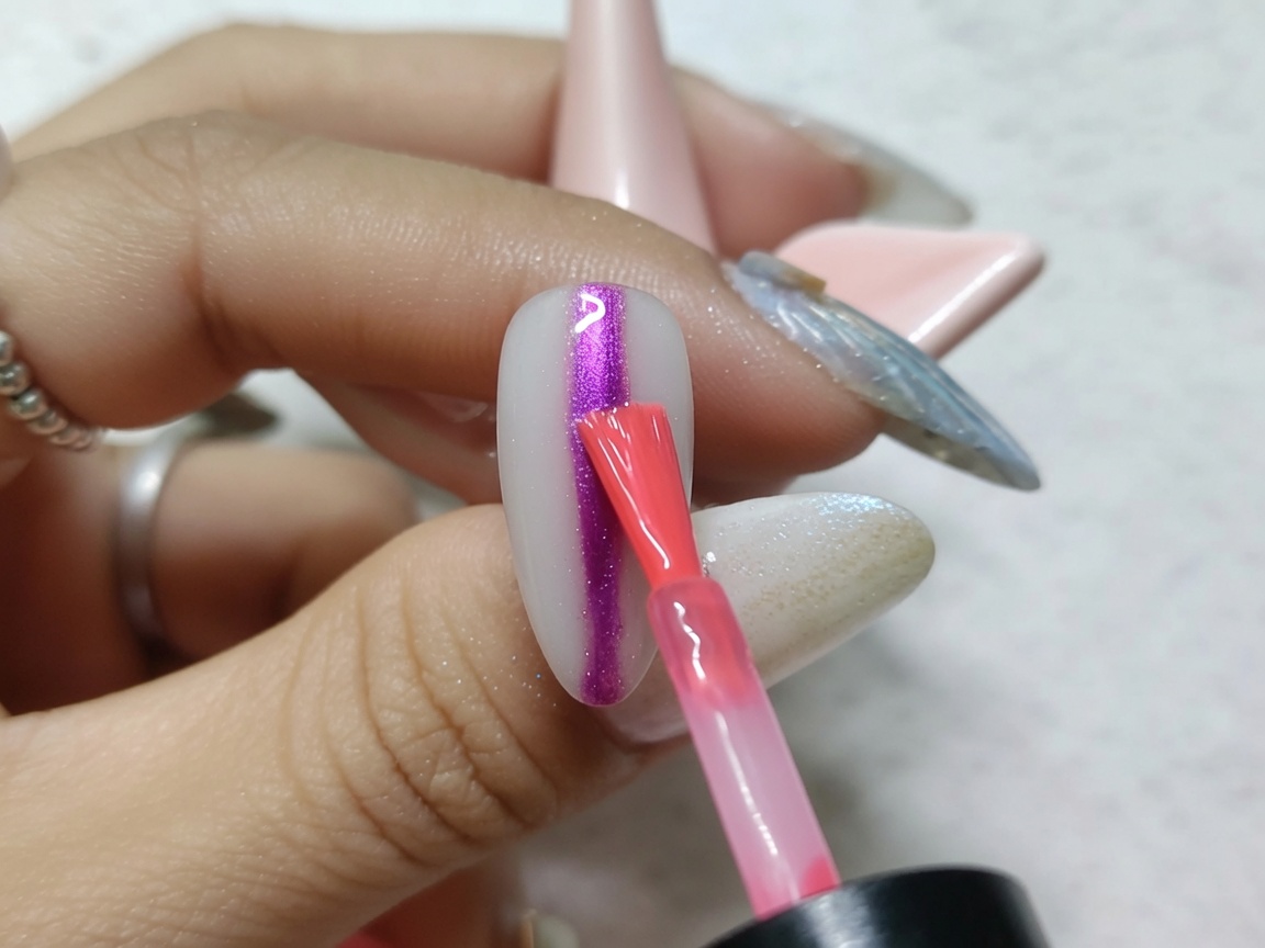 Ein Nailart-Pinsel trägt einen kräftigen, vertikalen Strich aus hellroter Aquarell-Tinte auf die Mitte eines metallischen Nagels auf.