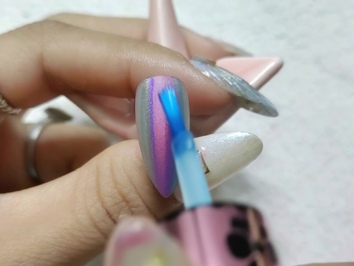Eine Nahaufnahme eines Pinsels, der die nassen Kanten der roten und blauen Tinte auf einem Chrome-Nagel verblendet.