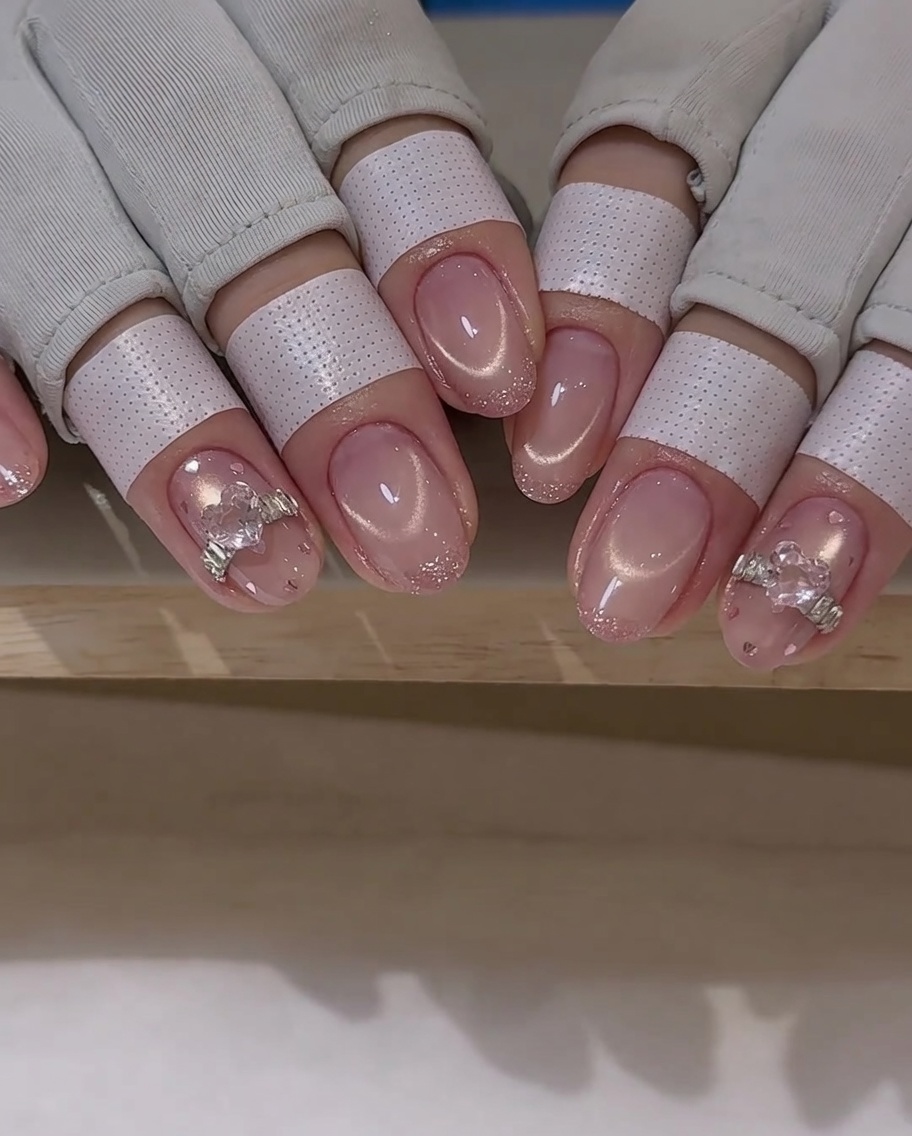 Ein Nailart-Pinsel trägt eine dünne Schicht Top Coat um einen Kristall-Charm auf einem Nagel auf.