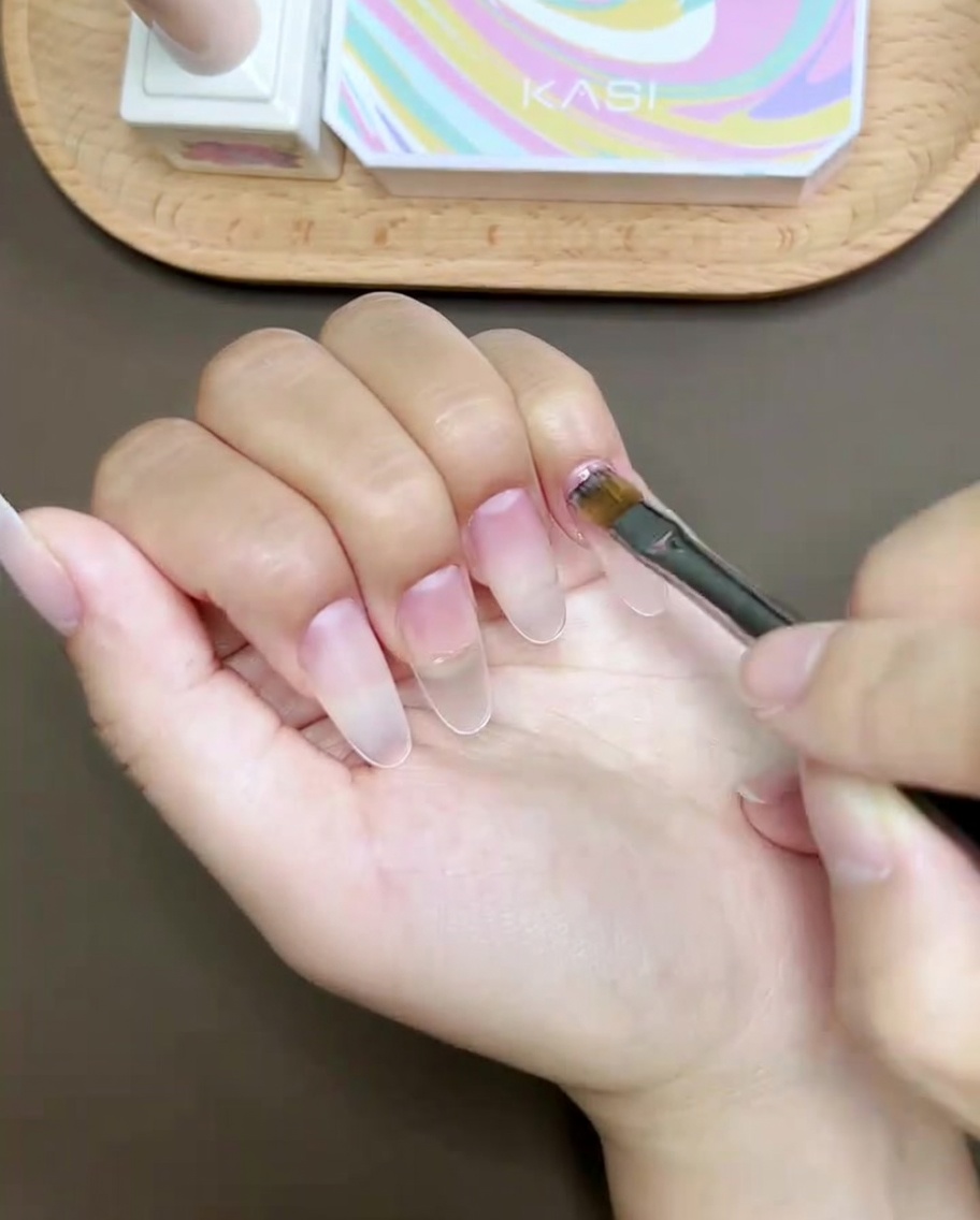 Ein Nagelpinsel zieht eine rosa geschwungene Linie an der Daumenspitze.