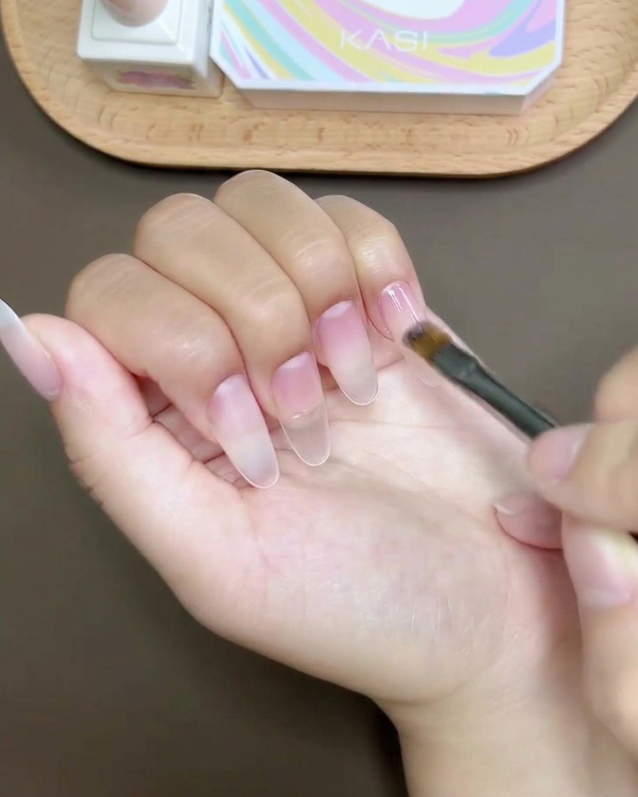 Ein Gel-Pinsel trägt glänzenden Top Coat über das fertige Nageldesign auf.