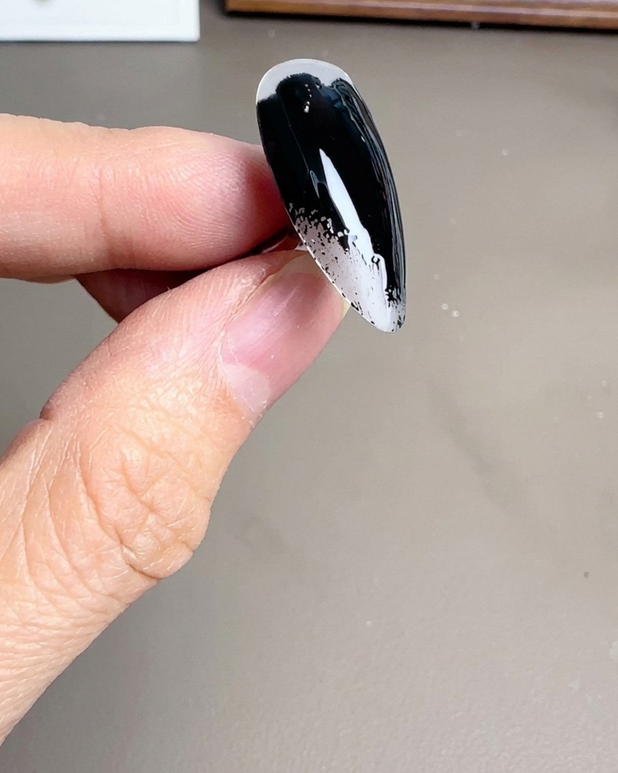Ein Pinsel trägt schwarzen Gellack auf eine klare Stiletto-Nagelspitze auf.