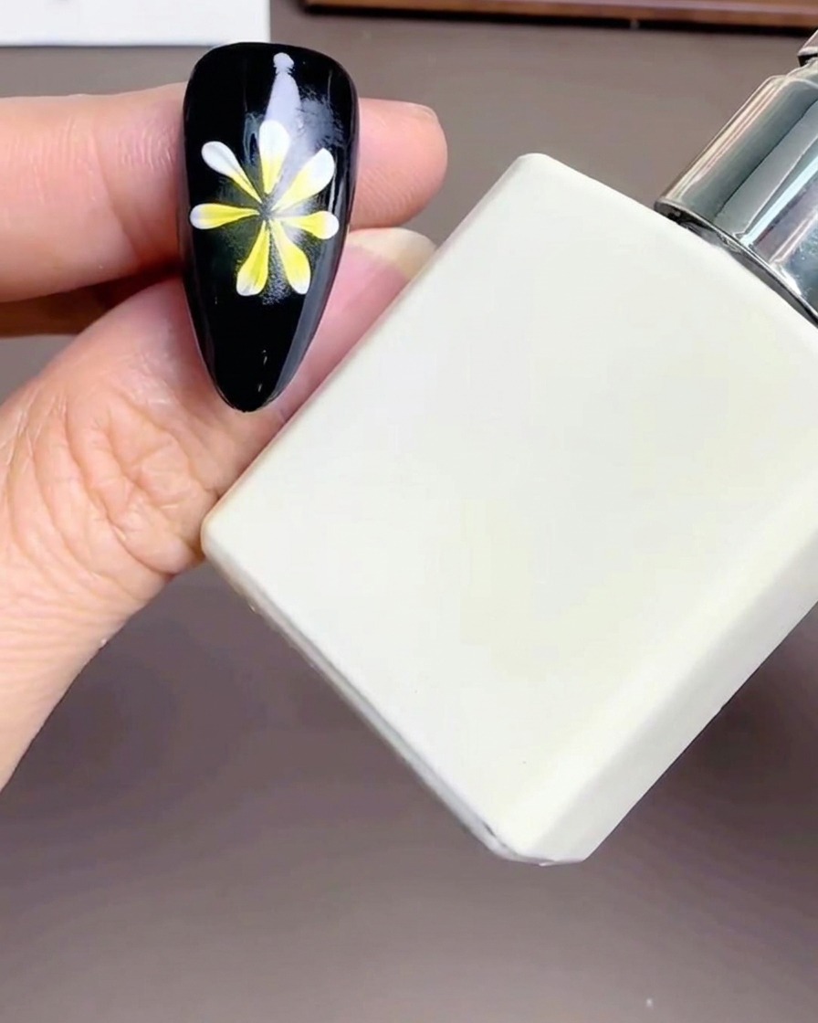 Eine weiße rechteckige Flasche Diamond Top Coat neben einem Nagel mit Blumendesign.