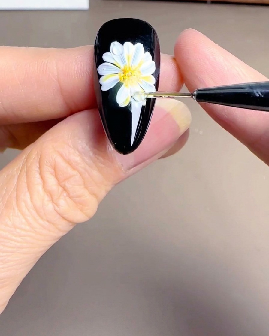 Nahaufnahme des Zentrums eines gemalten Gänseblümchens auf einem Nagel mit winzigen weißen Punkten als Detail für den gelb-orangenen Kern.
